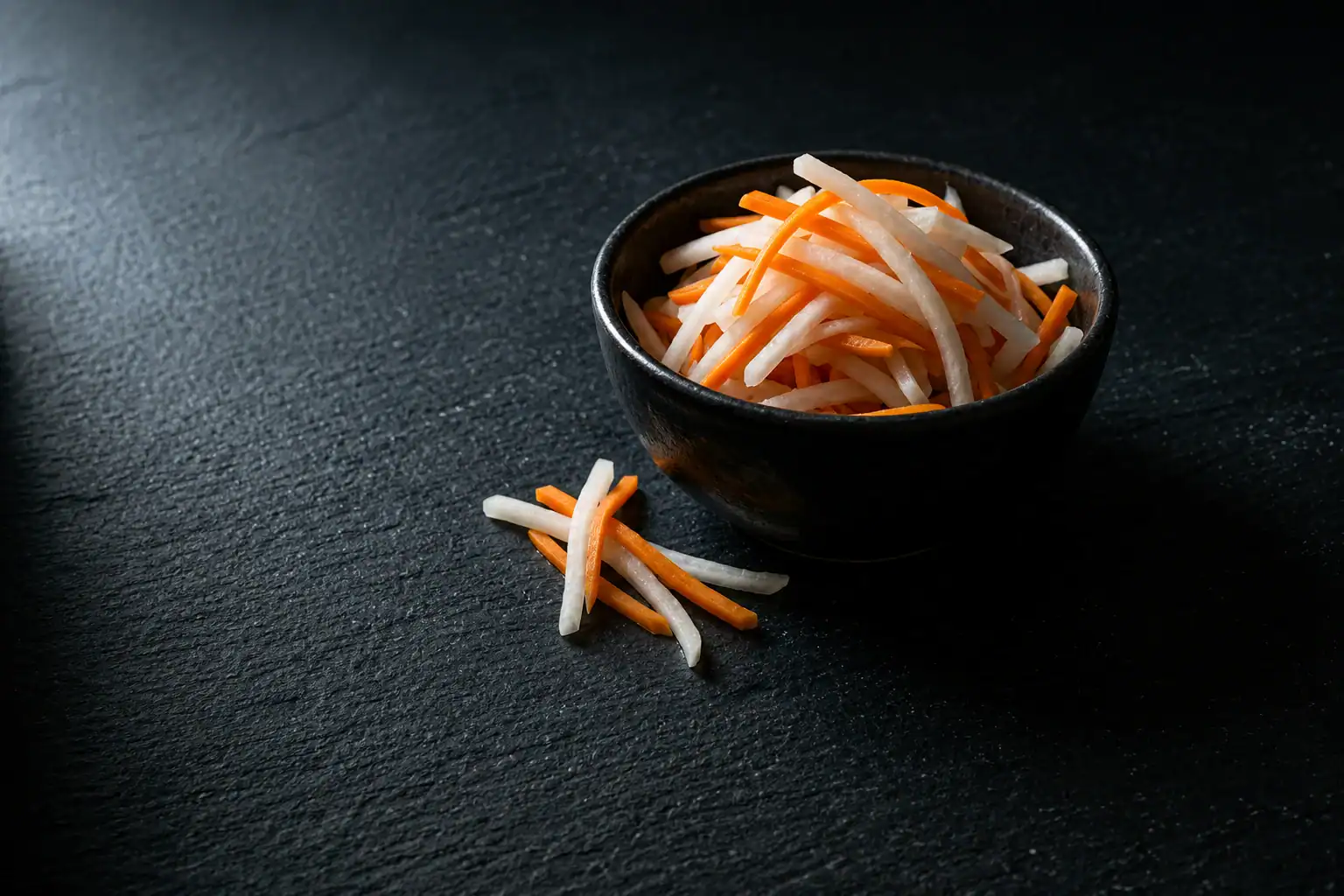 Đồ Chua Vietnamese pickled daikon and carrot julienned in dark ceramic bowl on slate
