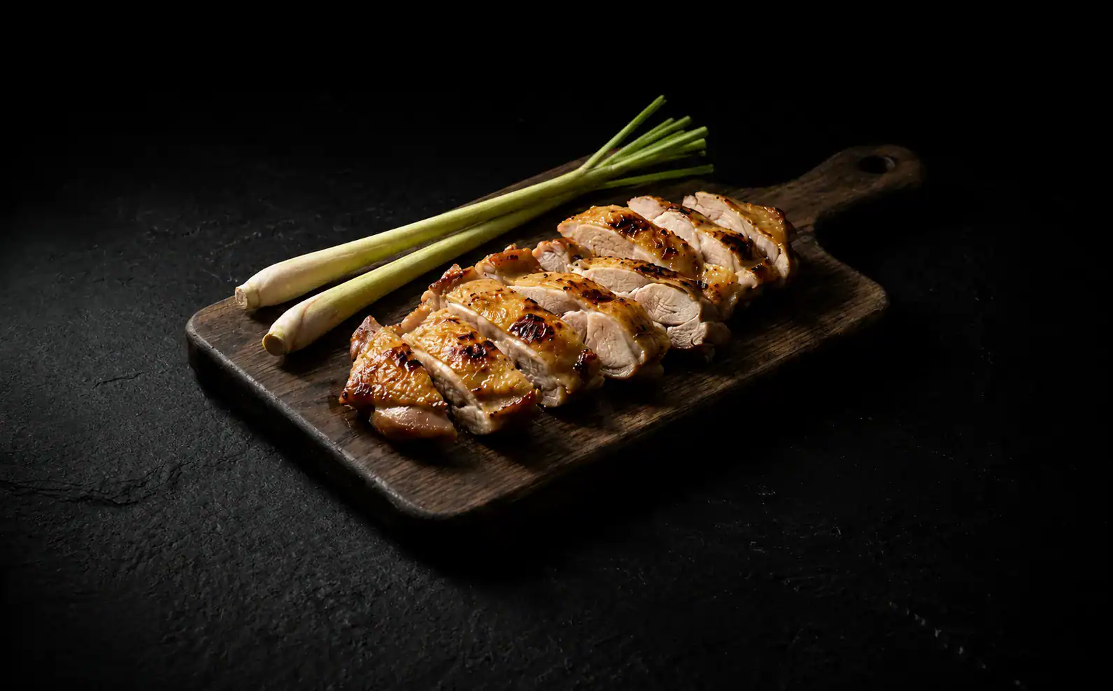 Lemongrass chicken thighs sliced on a wooden cutting board with dark slate background